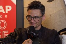 Sam Feder photographed while seated and engaged in an interview. Sam is a white person with short hair and glasses. They are wearing a leather motorcycle jacket on top of a dark shirt.