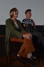 Kate Bornstein, a white person with a short bob hairstyle and round glasses, sits to the left of Sam Feder and laughs. Sam Feder, a white person with short coiffed hair, sits with microphone in hand while answering questions after a film screening.