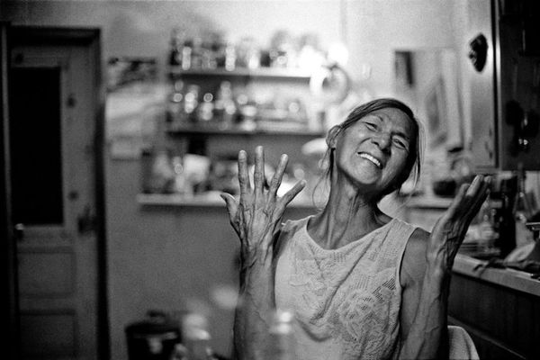 Aiyyana Maracle smiles and throws up her hands in possibly an expression of joy. The portrait is monochrome and the background, while blurry, suggests an interrior space such as a kitchen or studio. Aiyyana is Indigenous, has her hair pulled back and wears a sleeveless top with a subtle floral design.