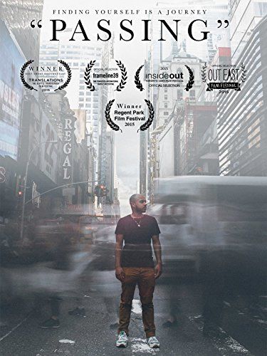 Long exposure image of a Black trans man standing in the middle of a busy city crosswalk with blurred traces of cars and people behind them. They have medium brown skin, a short buzzed hair cut with dark brown facial hair, and are wearing a maroon t-shirt, brown jeans and statement sneakers.