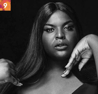 Fatima Jamal is a Black Trans woman with dark brown skin. She is shown from the chest up in a black and white filter. They have long black hair, they have eyeliner and are in front of a black background. They have their hands posed, one with the back of the hand pressed against the cheek and the other touching the lower part of her hair.