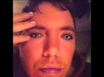 A person looks into a front facing camera screen. Their face has computer-generated filters imposed overtop that change the lip shade, foundation or skin colour and eye colour, eye makeup, and nails. The person has short hair, fair skin and wears a hoodie.