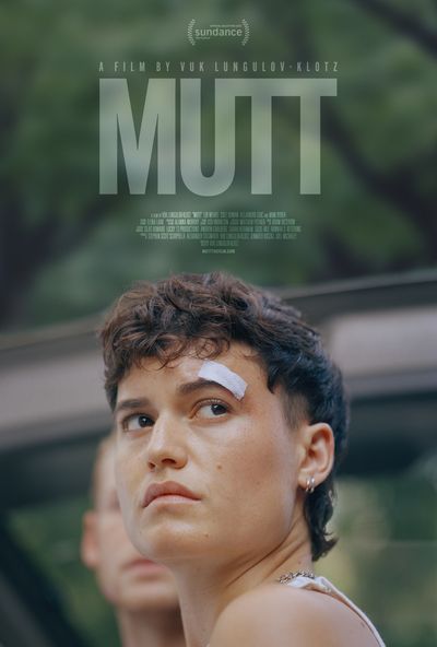 A portrait of a young trans man. The person is a fair-skinned person with a golden tan and warm brown hair in a soft mullet fashion. They have very small silver double hoop earrings and a silver necklace that is somewhat covered by the angle of their shoulders and a white tank top. The natural forest background is blurred into soft calming colours. The film title is written in a very low opacity to allow for the emotional portrait to be the focal point.