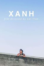 A person leaning on a concrete wall with a skyline above them.They have light brown skin with tattoos on their right arm. They are wearing a black tank top and a gold chain around their neck. They have short light blue hair and are wearing lipstick looking off to the left. In the skyline above the person, white text reads "XANH: film directed by Sal Tran."
