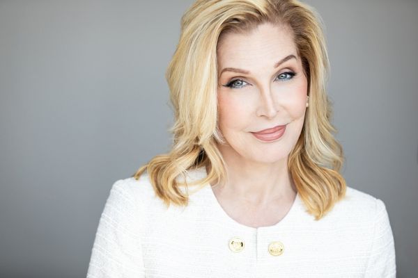 Studio portrait of Bianca Leigh from the chest and above in front of a light grey studio backdrop. Bianca has pale skin and blue eyes, and blonde shoulder length hair. She is wearing white blouse and light earrings.